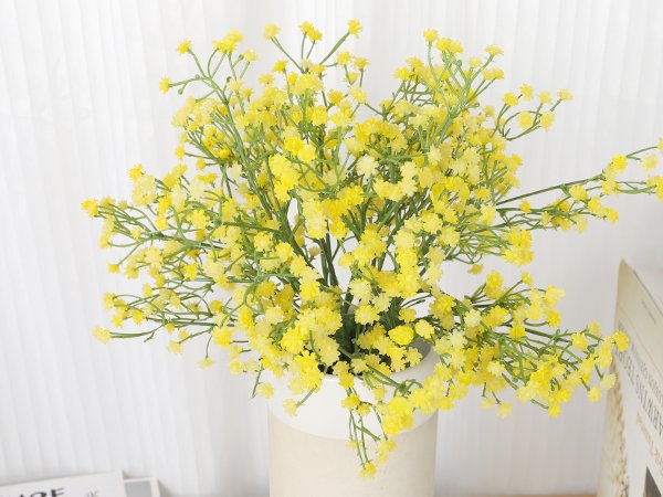 Yellow artificial baby's breath bouquet in a vase against a white curtain background