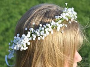Blonde woman wearing a white artificial baby's breath flower crown with green grass background
