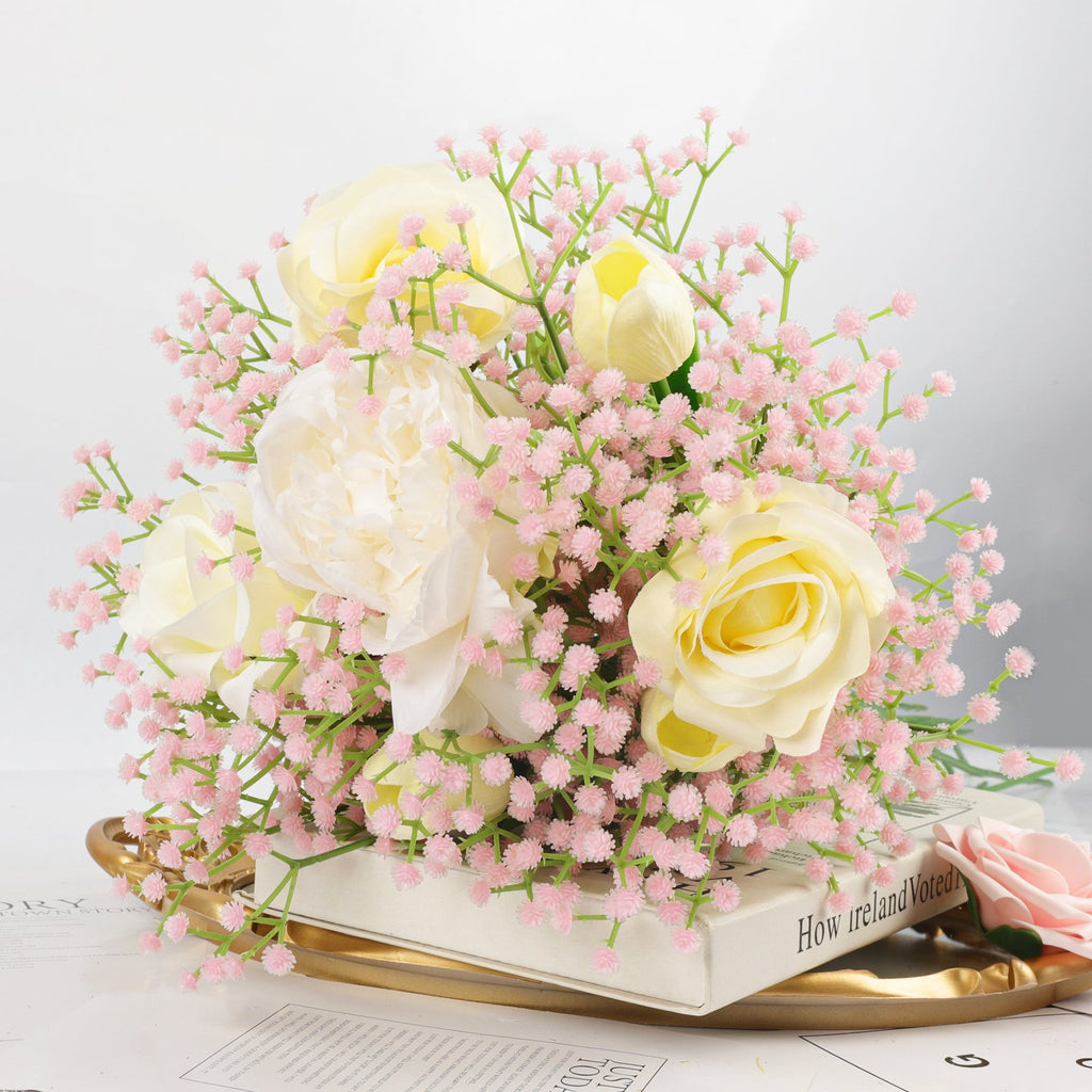Artificial baby's breath and rose bouquet with pink flowers and yellow roses on a gold tray with books.