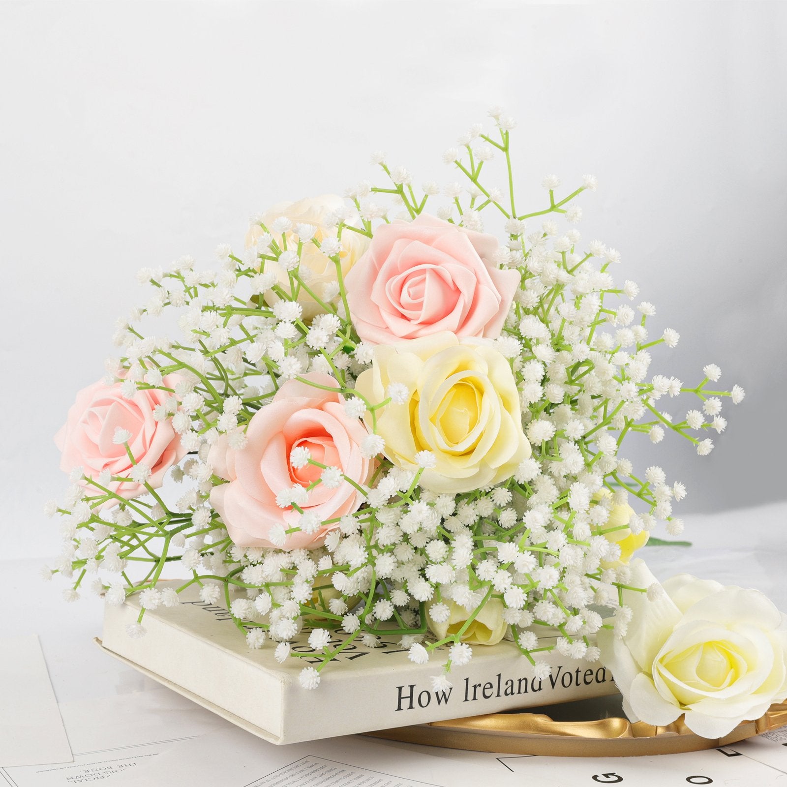 Bouquet of pink and yellow artificial roses with baby's breath on a book