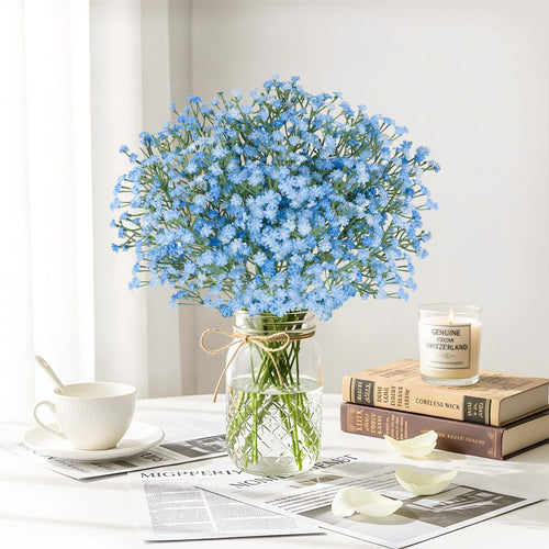 Blue artificial baby's breath bouquet in a glass vase with a cup and books on a table