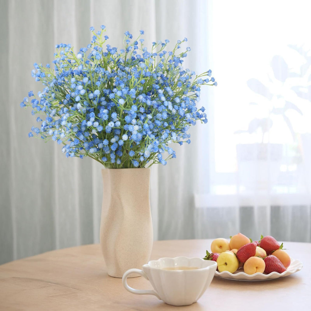 Blue artificial baby's breath bouquet in a vase on a table with a fruit bowl and teacup