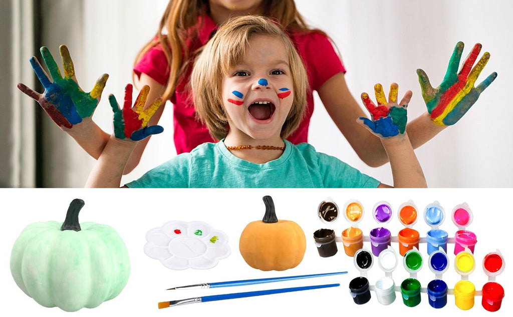 Two children with colorful paint on their hands and faces, with a pumpkin decorating kit laid out below.