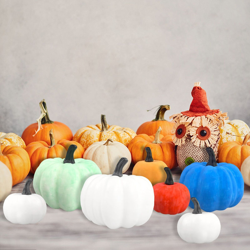 Assortment of decorative pumpkins in various colors including white, green, orange, red, and blue, with a scarecrow figure in the background.