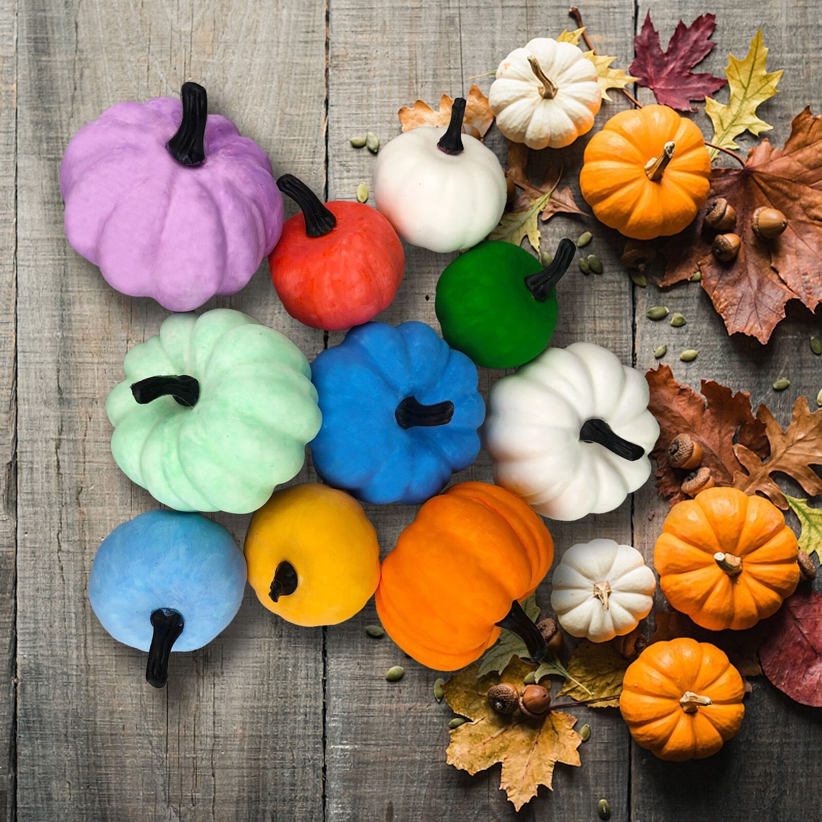 Assortment of colorful decorative pumpkins and autumn leaves arranged on a rustic wooden surface.