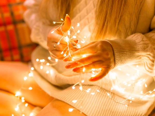 Close-up of hands holding warm white LED fairy lights with silver wire, soft focus background
