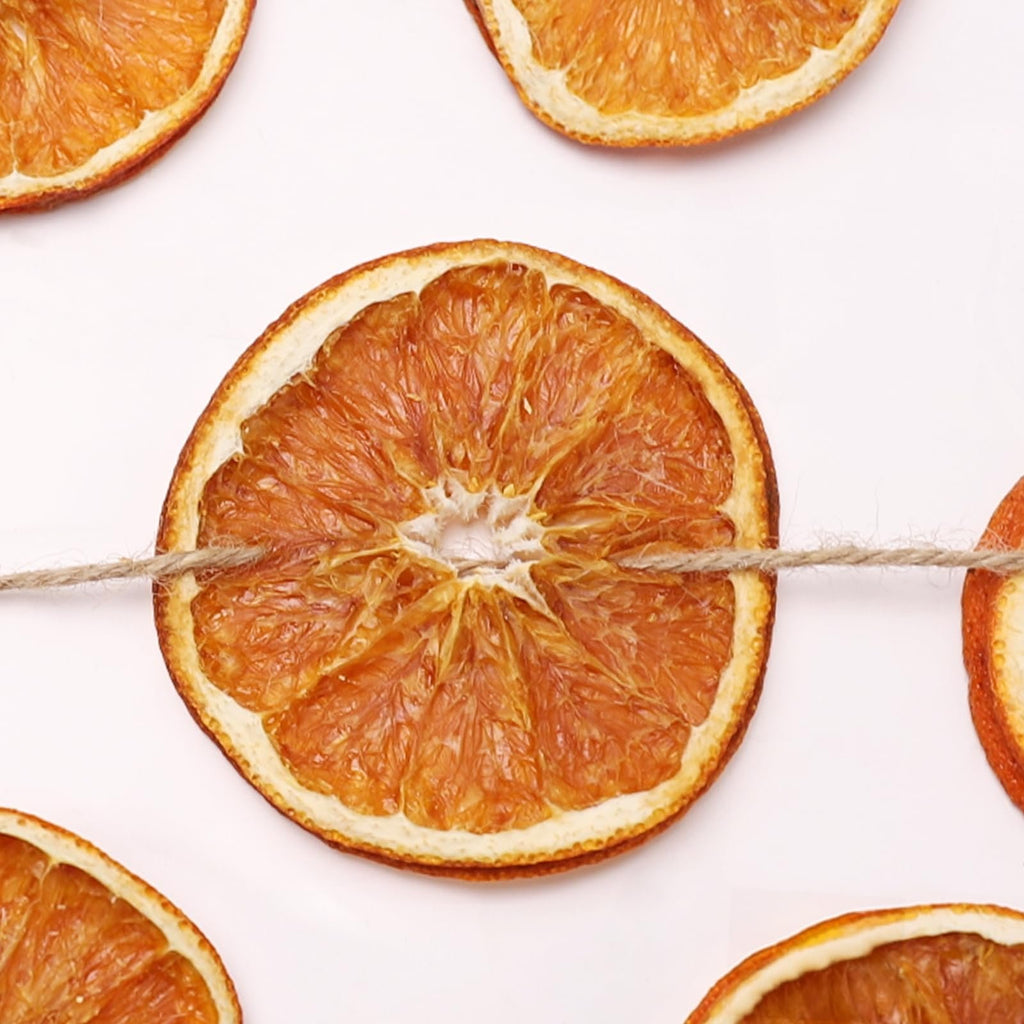 Dried orange slices strung on jute twine against a white background, close-up view.