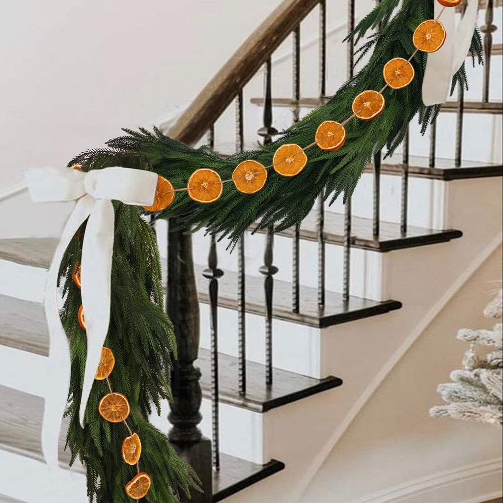 Dried orange slice garland draped on a staircase with green garland and white bows