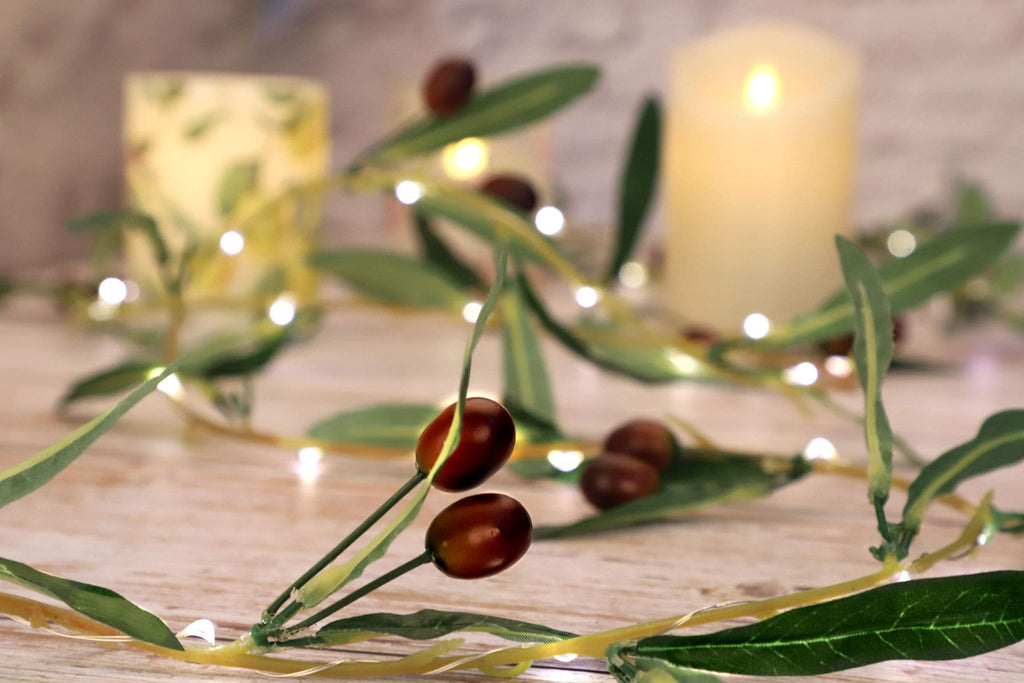 Olive branch garland with warm white LED lights and faux olive fruits, set against a blurred background with candles.