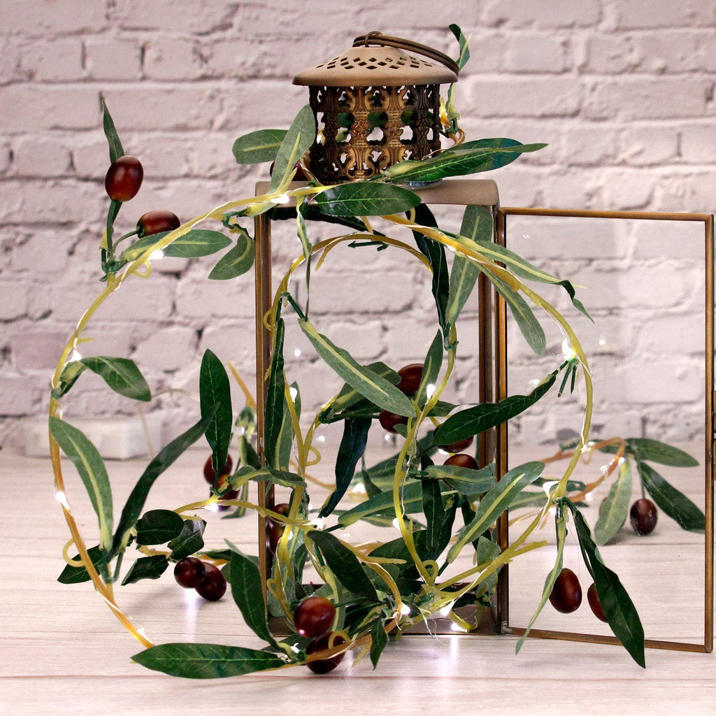 Olive branch garland string lights with warm white LEDs and faux olives draped around a decorative lantern and a glass frame.