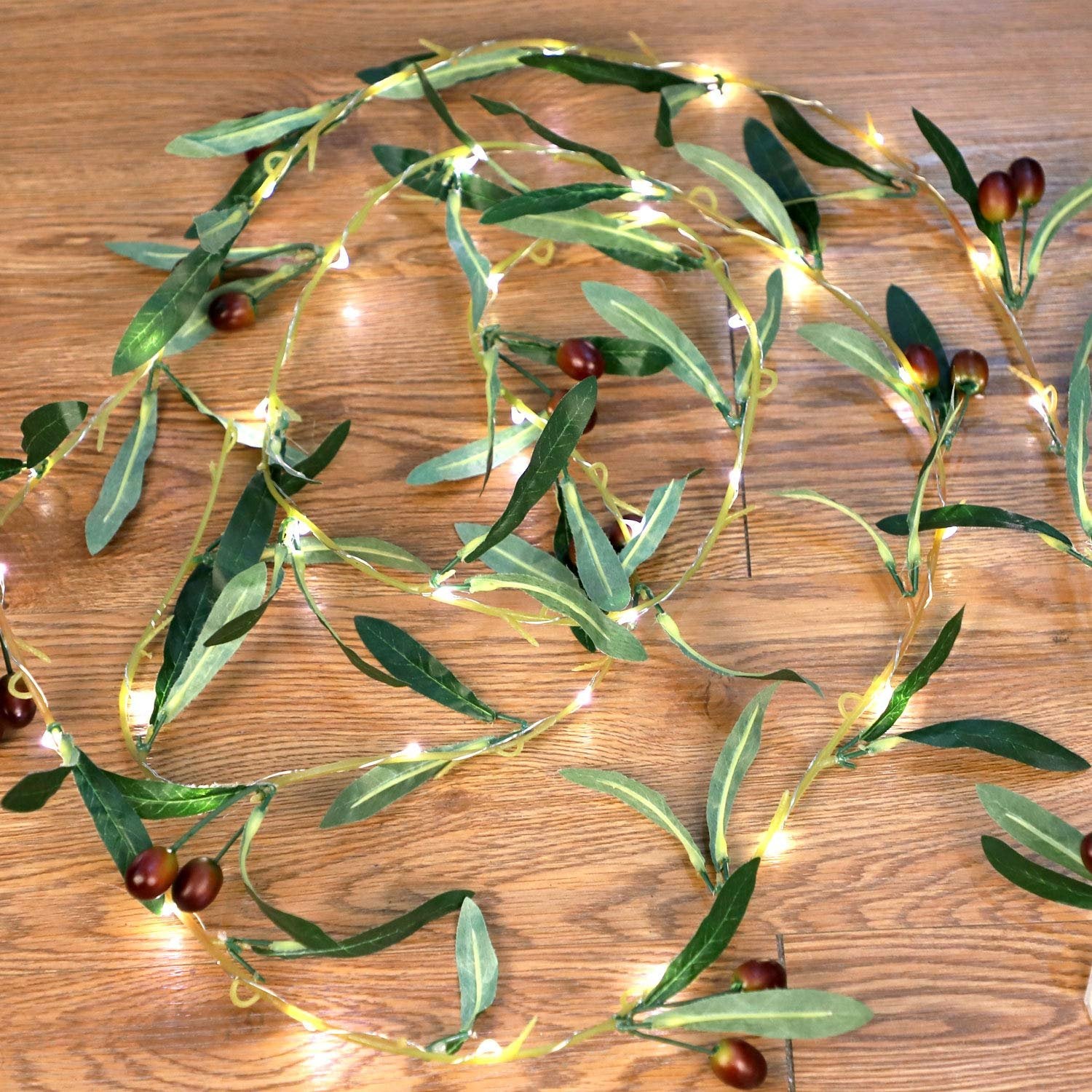 Olive branch garland string lights with warm white LEDs and faux olive fruits on a wooden surface.