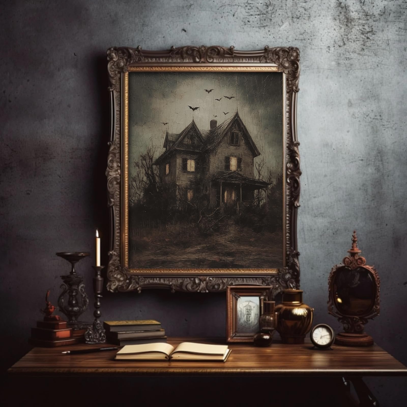 Framed dark Halloween art print of a haunted house with bats flying in a cloudy sky, displayed on a table with books and a candle.