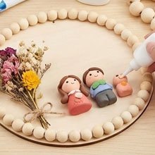 Unfinished wood circle craft project with clay figures and dried flowers, being assembled with glue