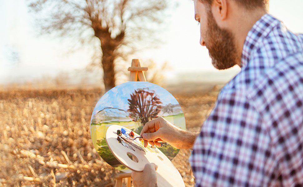 Man painting a landscape on a round canvas outdoors with a palette in his hand