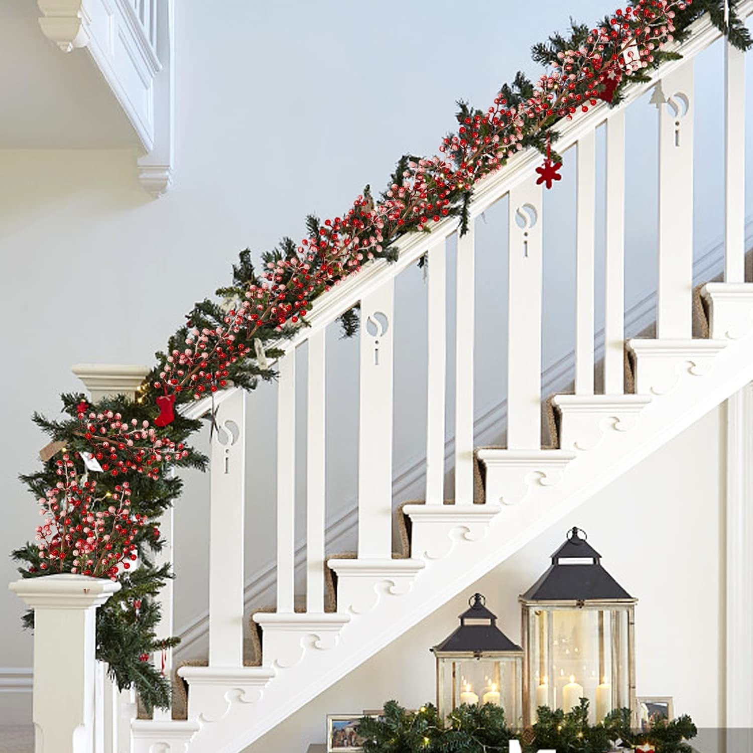 Christmas garland with red berries and pine branches draped on a white staircase railing with lanterns below.