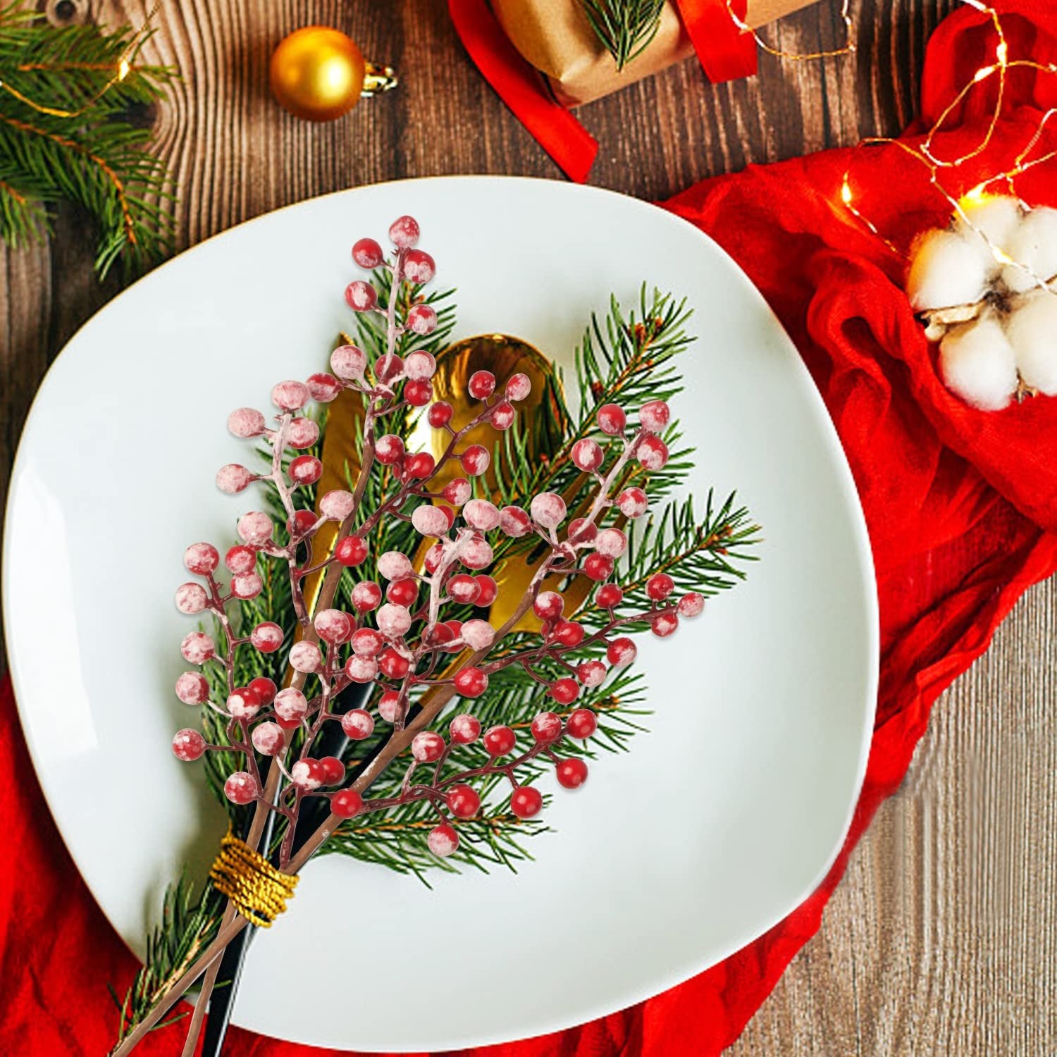 Christmas berry stems with pine sprigs arranged on a white plate with golden cutlery, set on a wooden table with festive decorations.