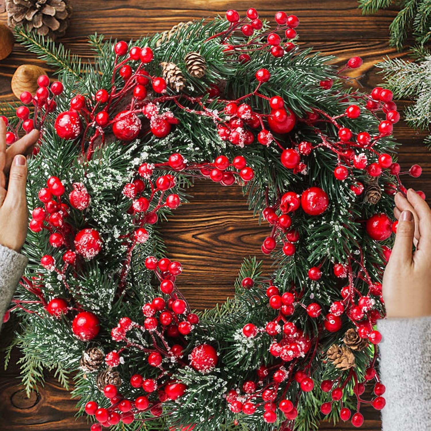 Christmas wreath with red berries and pine cones, hands adjusting the wreath on a wooden background.