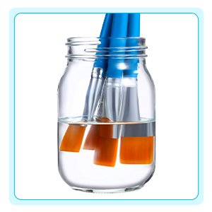 Three flat nylon paint brushes with orange bristles soaking in water inside a glass jar.