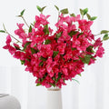 Artificial pink bougainvillea flower vines with green leaves in a white vase.