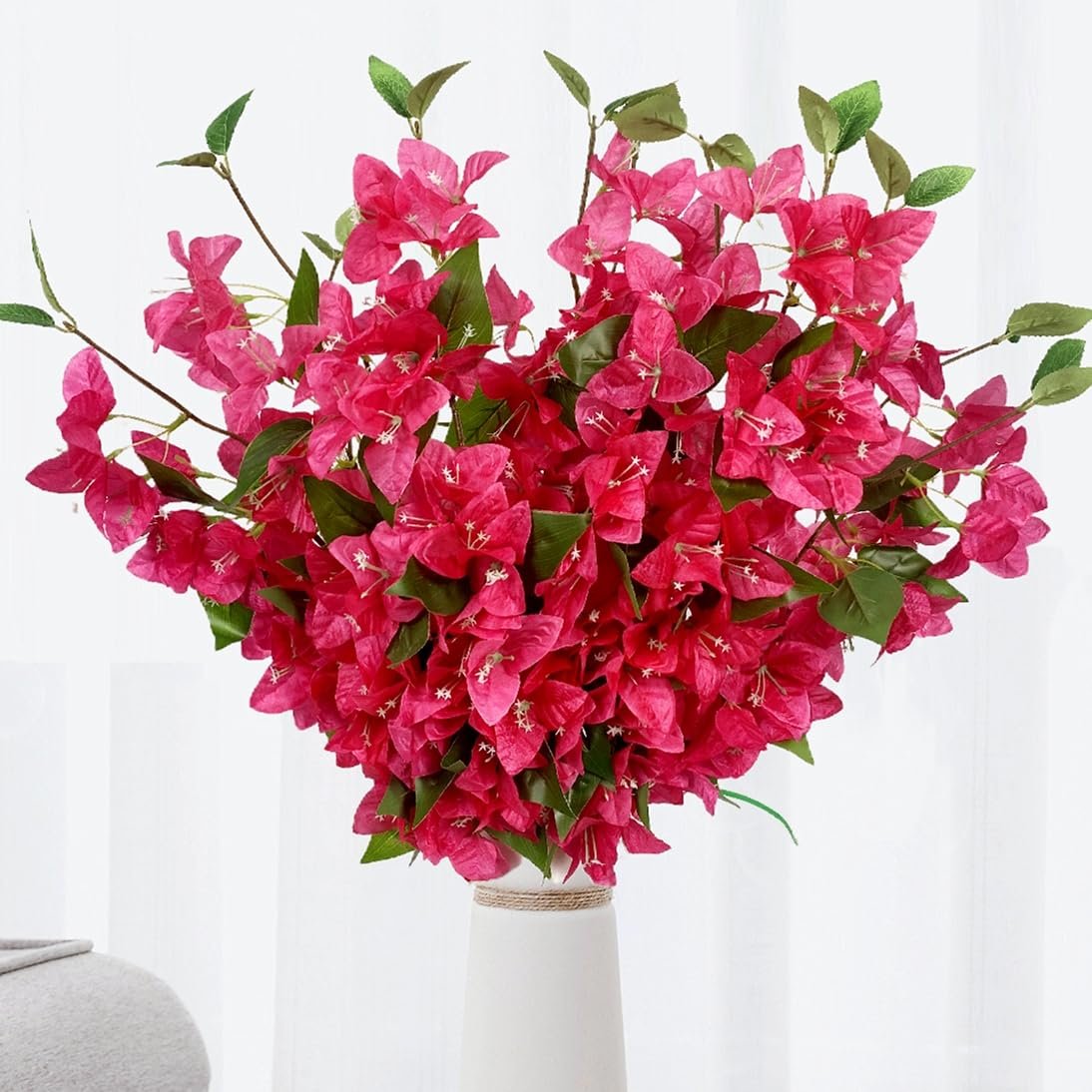 Artificial pink bougainvillea flower vines with green leaves in a white vase.