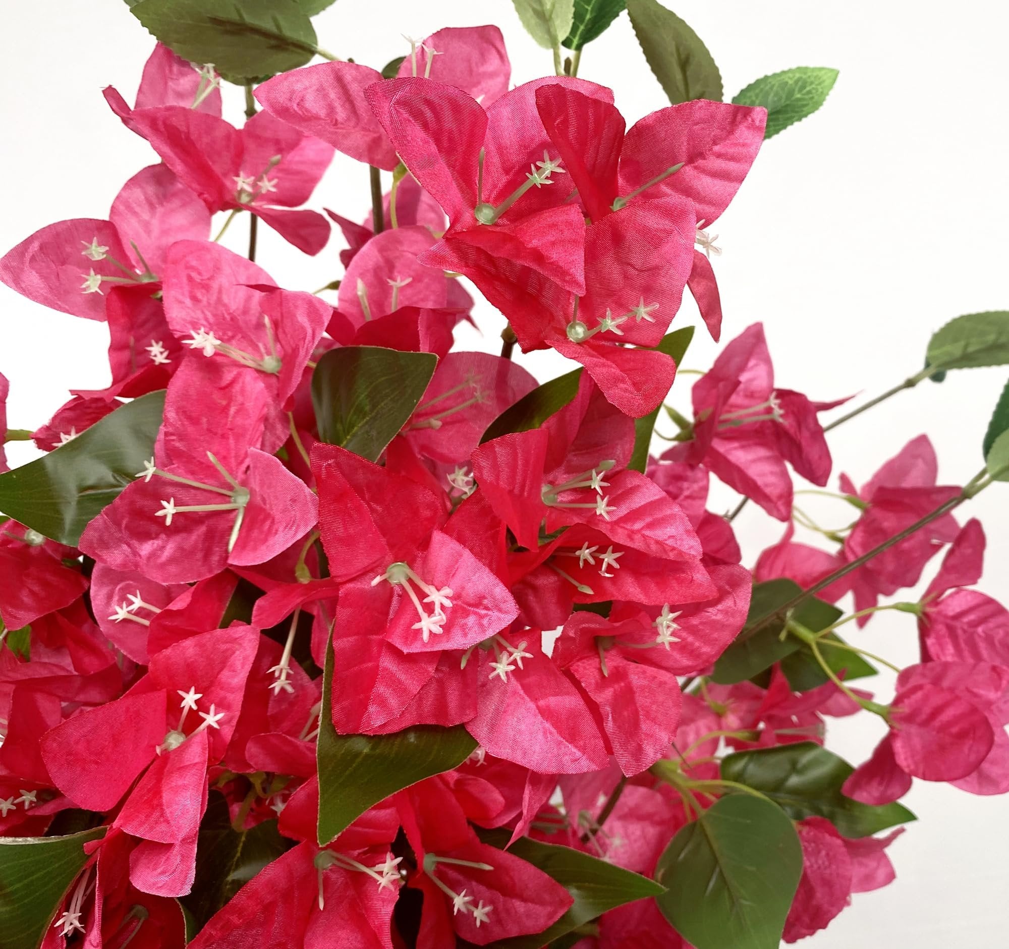 Close-up of artificial pink bougainvillea flower vines with green leaves against a white background.