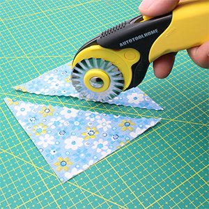 Hand holding a pinking rotary cutter cutting patterned fabric on a green cutting mat
