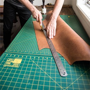 Person cutting brown leather with a rotary cutter and ruler on a green cutting mat