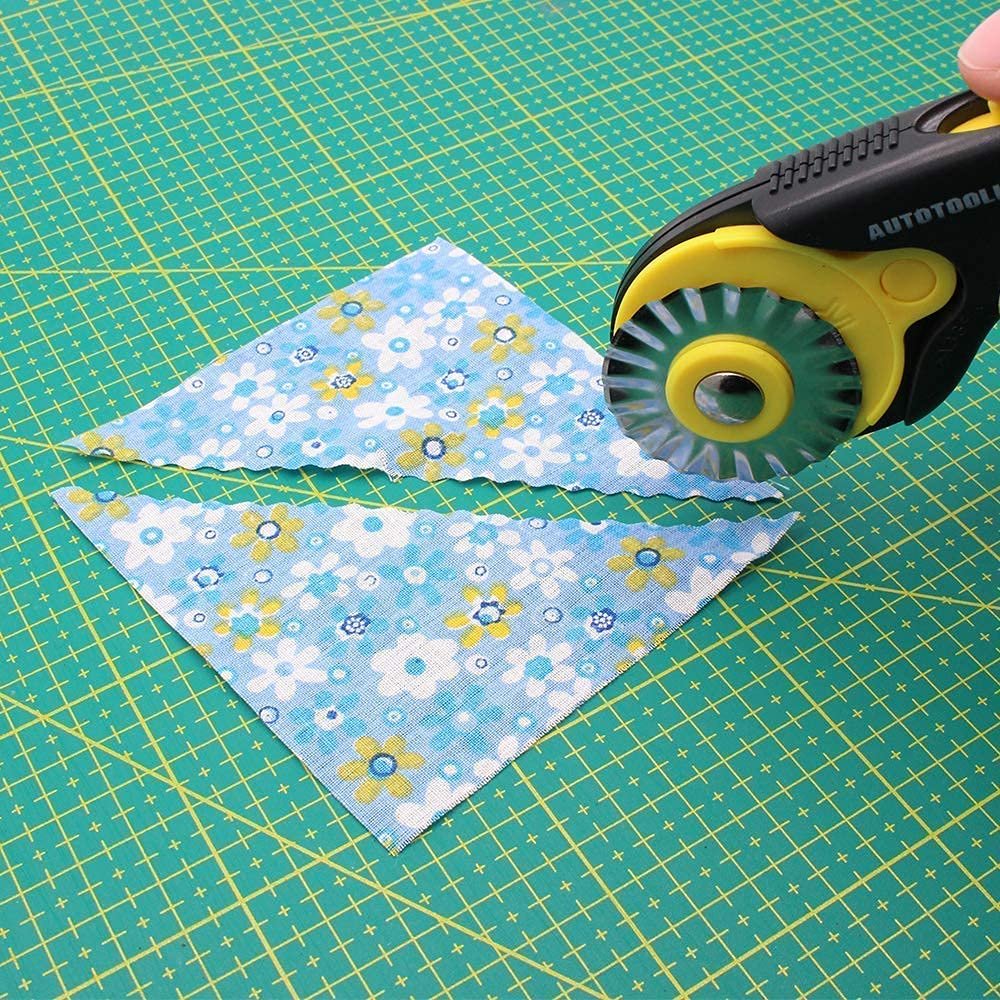 Rotary cutter with pinking blade cutting blue floral fabric on a green cutting mat