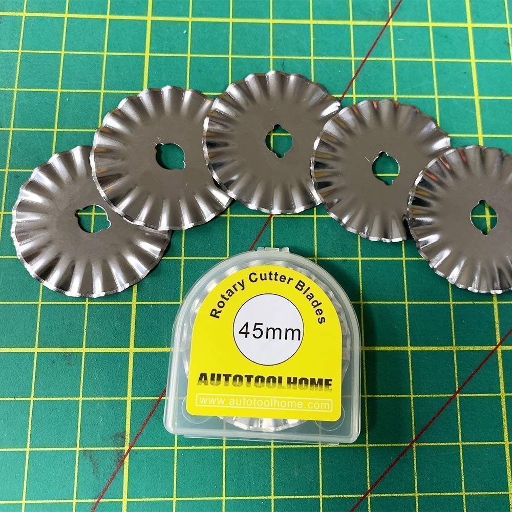 Five 45mm pinking rotary cutter replacement blades arranged around a clear storage case on a green cutting mat.