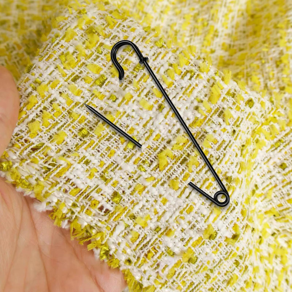 Black extra large safety pin with locking design on textured yellow and white fabric held by a hand