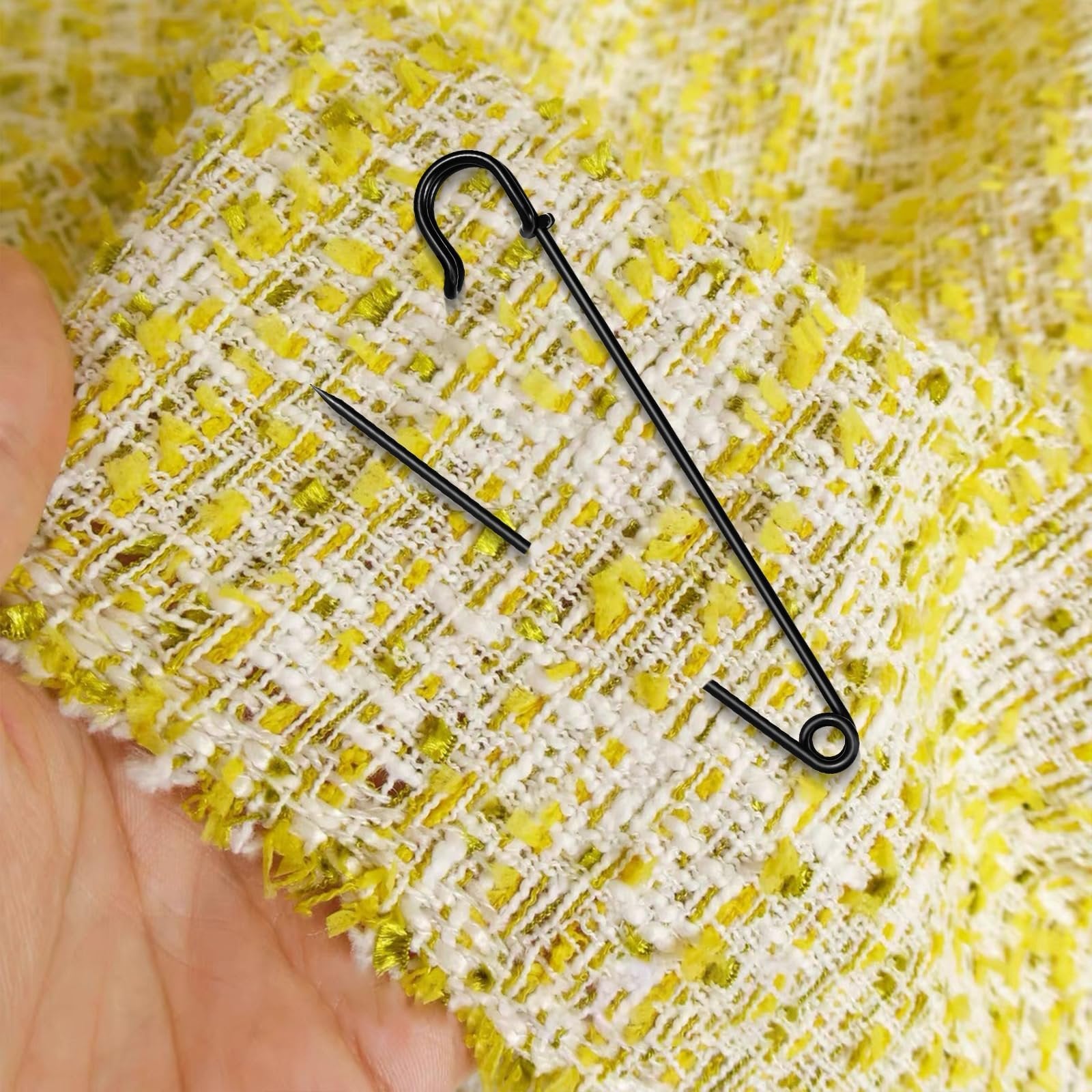 Black extra large safety pin with locking design on textured yellow and white fabric held by a hand