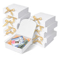 Stack of white gift boxes with gold ribbon bows, one box open showing contents like handkerchiefs, a bow tie, and a small pink item.