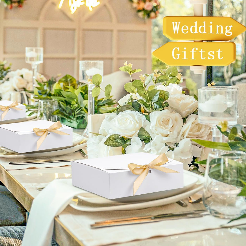 White paper gift boxes with gold ribbon tied on a table setting with floral arrangements.