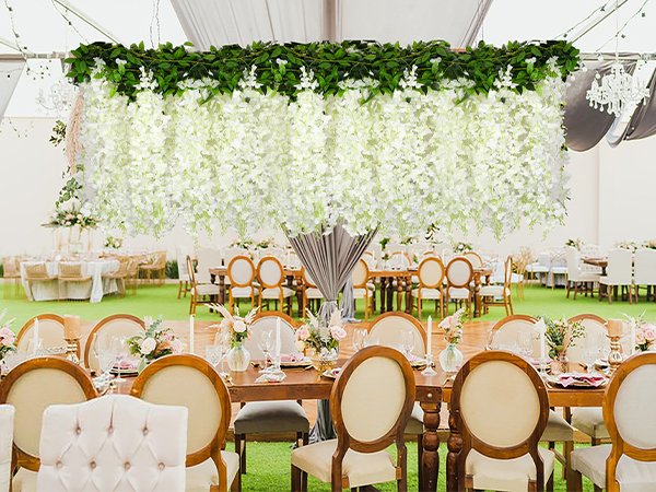 White artificial wisteria garland with green leaves draped over a wedding reception venue with tables and chairs