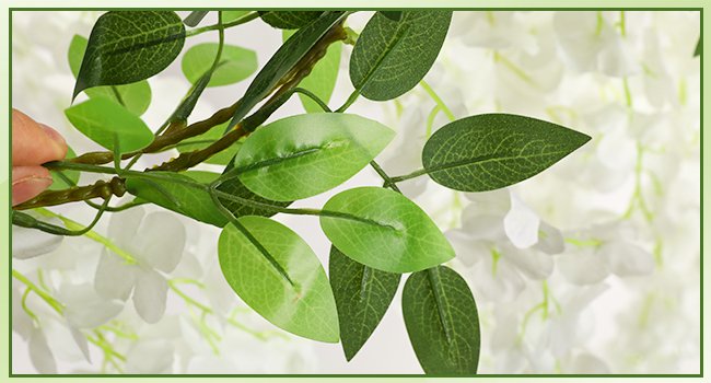 Close-up of artificial white wisteria garland with green leaves and a hand holding a stem.