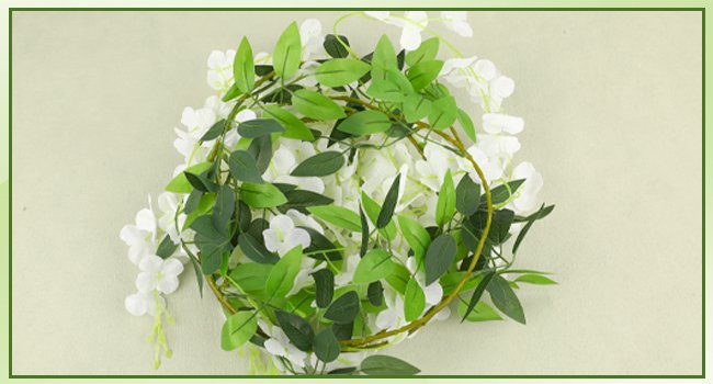 White artificial wisteria garland with green leaves, coiled on a light background.