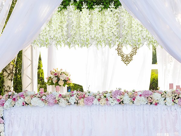 Wedding reception table decorated with white and pink flowers and draped white fabric.