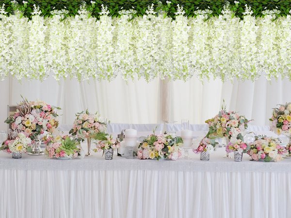 White artificial wisteria garlands draped above a decorated table with floral arrangements.