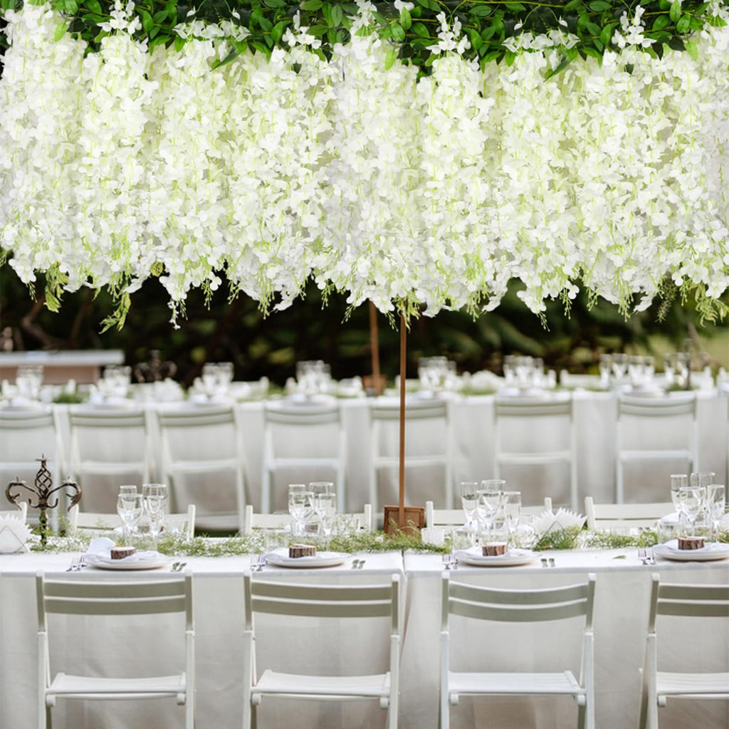 White artificial wisteria garlands draped over a formal outdoor dining table setting with white chairs and place settings.