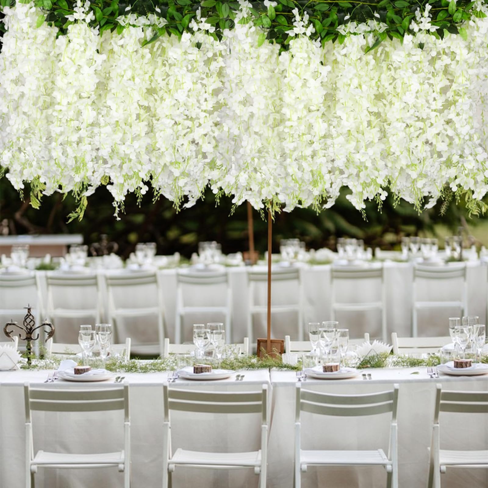 White artificial wisteria garlands draped over a formal outdoor dining table setting with white chairs and place settings.