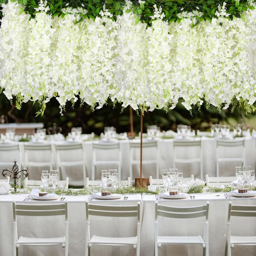 White artificial wisteria garlands draped over a formal outdoor dining table setting with white chairs and place settings.
