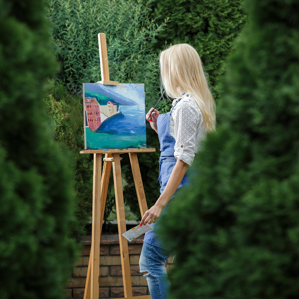 Woman painting a landscape on an easel outdoors, surrounded by greenery