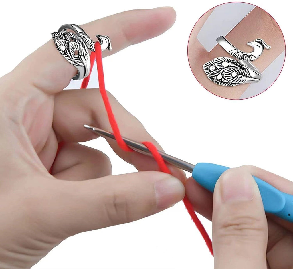 Close-up of a hand demonstrating a silver adjustable crochet loop ring with a feather design, guiding red yarn for knitting tension control.