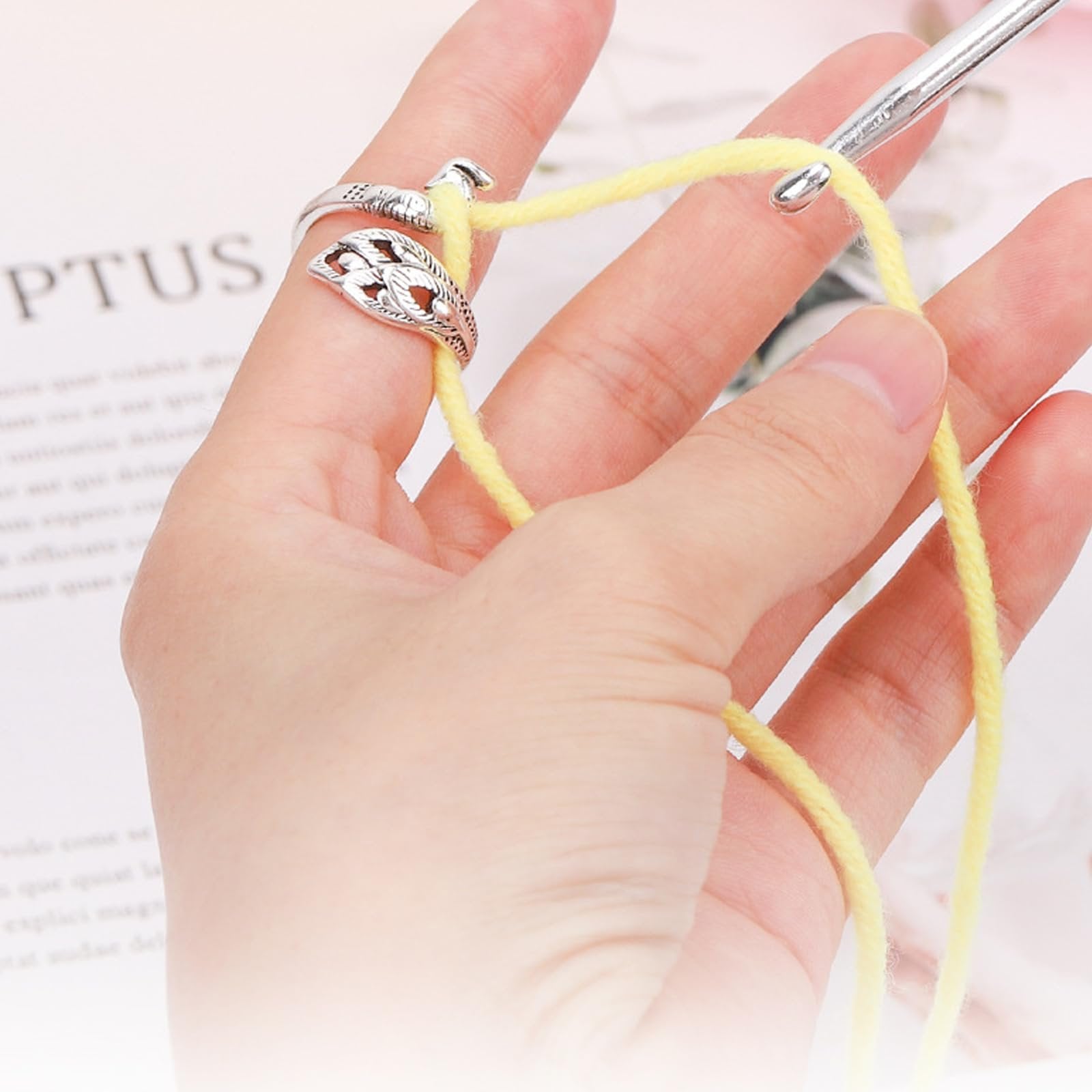 Close-up of a hand wearing an adjustable crochet loop ring and holding yellow yarn with a crochet hook.