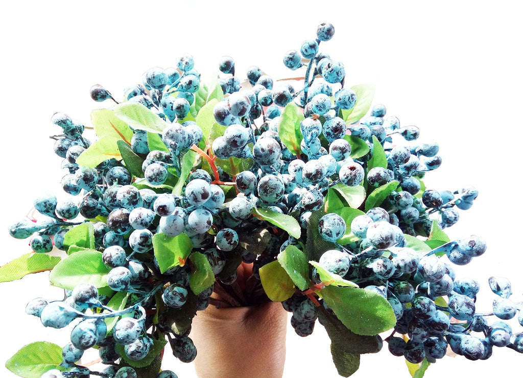 Close-up of artificial blueberry stems with green leaves, held by a hand against a white background.