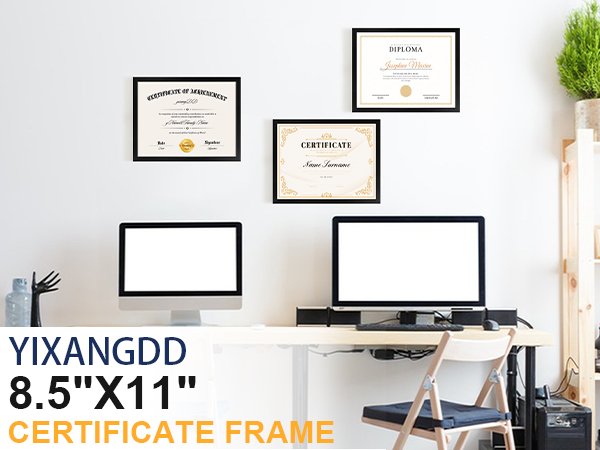 Three black certificate frames on a wall above a desk with two computers and a plant.