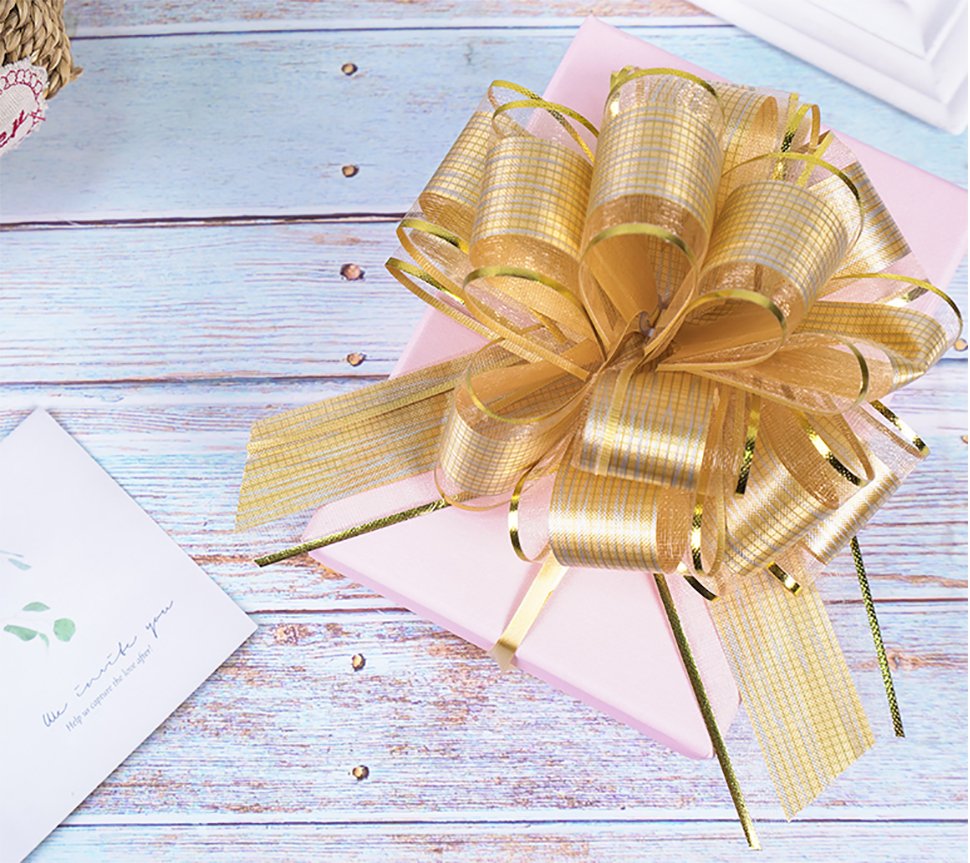 Gold pull bow on a pink gift box with a card on a wooden surface