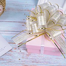 Gold pull bow on a pink gift box with a white ribbon, set on a light blue wooden surface with a white card.