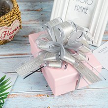 Pink gift box topped with a silver pull bow, with a white photo frame and woven basket in the background.