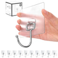 Hand holding a transparent adhesive wall hook with a silver hook, showing the product and packaging.